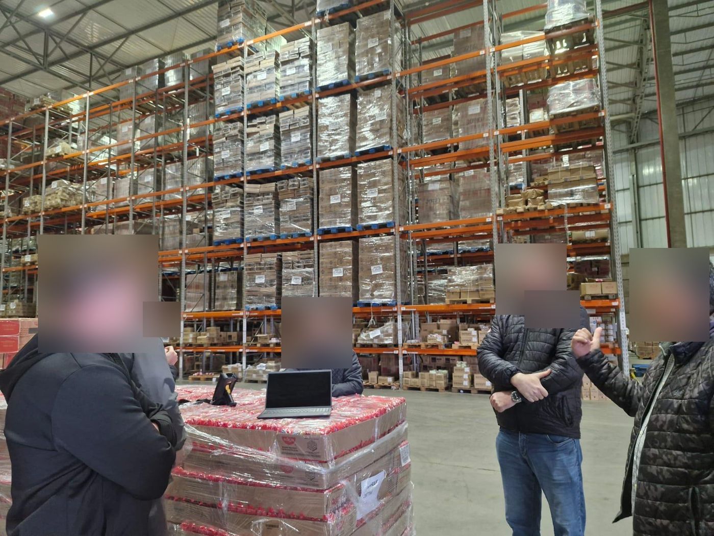 Equipe em reunião de gemba no meio do armazém, em frente aos porta-paletes carregados